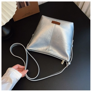 Close-up of silver metallic crossbody bag featuring brown leather logo and stitching detail