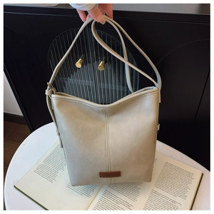 Close-up of beige faux leather tote bag with vertical stitching and brown brand tag