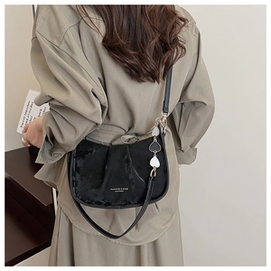 Détail du sac bandoulière demi-lune noir avec plis et pendentif décoratif en cœur
