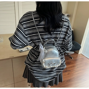 Détail d'un sac à dos argenté métallisé avec bordure en dentelle blanche et pendentif