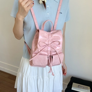 Pink faux leather backpack with bow detail and drawstring closure worn by a model