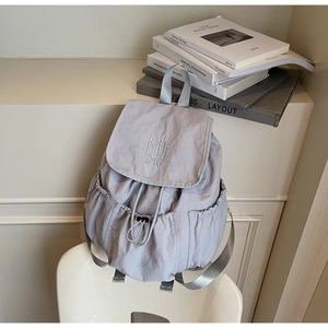 Close-up of light grey nylon backpack showing drawstring closure and MUTING embroidery