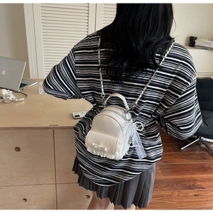 Gros plan d'un mini sac à dos blanc avec dentelle, détail de nœud et fine chaîne en métal