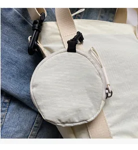 Close-up of cream round mini accessory pouch with black hook on denim background