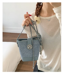 Detail of light blue denim texture bucket bag featuring silver turn-lock and chain strap
