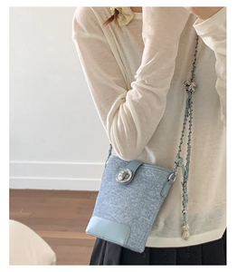 Detail of light blue textured bucket bag with silver twist lock and chain strap