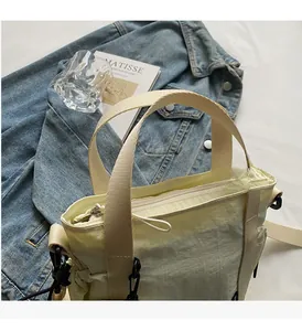 Close-up of beige nylon crossbody bag with wide webbing handles and side metal hook detail