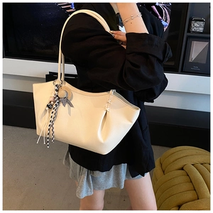 Detailed view of cream leather tote bag with elegant pleated sides and decorative charms