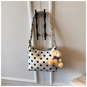 Gepunktete Schultertasche mit braunem Bären-Plüschanhänger an einem weißen Schrank