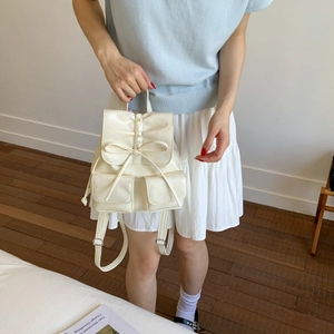Detail of cream white mini backpack featuring handmade bow accent and magnetic flap closure