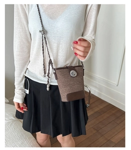 Detail of brown textured bucket bag with metallic twist lock and chain strap on model