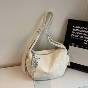 Close-up of cream crescent bag featuring glossy pleated leather and silver heart charm