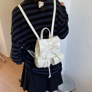 Detail of off-white backpack featuring pleated flap and decorative bow tie elements