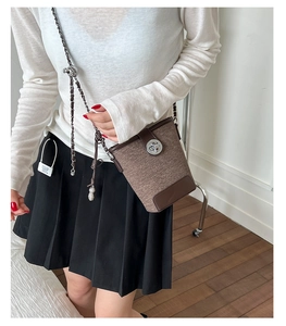 Detail of brown woven bucket bag featuring elegant leather strap and metallic lock closure