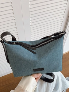 Borsa a tracolla in denim blu con manico in pelle nera e cerniera su sfondo bianco