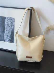 Minimalist cream-colored bucket bag with vintage leather logo and wide shoulder strap