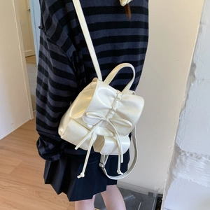 Detail view of cream leather backpack featuring drawstrings and bow accents on adjustable straps