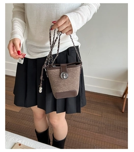 Detail view of brown tweed bucket bag with leather trim and silver metal twist lock