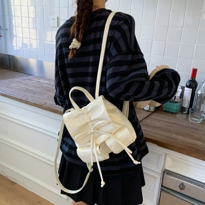 Side view of cream-white glossy backpack with bow ties and pocket details