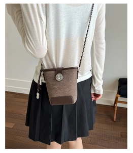 Detail of a brown bucket bag with metal lock, chain strap, and peanut-shaped charm accessory
