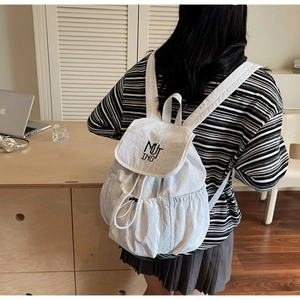 Detail of white nylon backpack featuring drawstring closure and MUTING embroidery