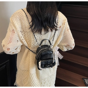 Détail d'un mini sac à dos en cuir verni noir avec dentelle blanche et breloque perle