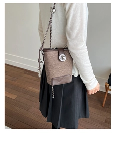 Detail of tweed bucket bag with brown leather trim and bear charm in lifestyle setting
