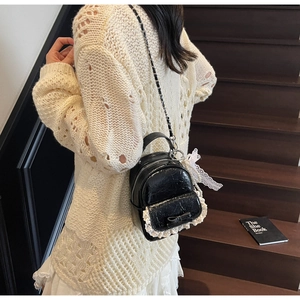 Détail d'un mini sac à dos en cuir noir avec bordure en dentelle blanche et nœud