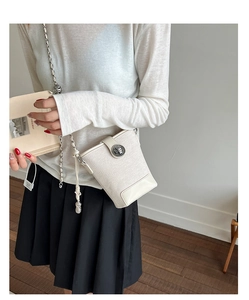 Detail of cream textured bucket bag featuring metal twist lock and chain strap on model
