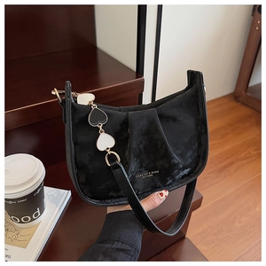 Détail du sac à bandoulière en daim noir avec chaîne cœur et logo dans un décor de café