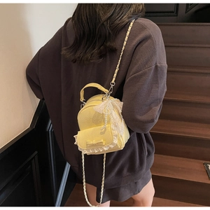 Detail of yellow bucket backpack with white lace, bow decoration and pearl pendant charm