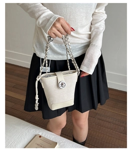 Chic white bucket bag with chain strap and tassel detail held by a model in casual attire