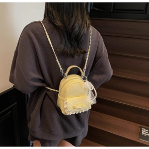 Détail d'un mini sac à dos jaune clair avec bordure en dentelle, perles et chaînes dorées