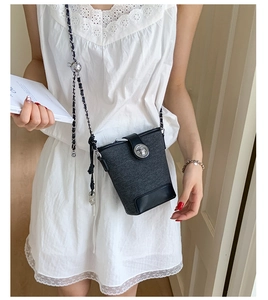 Detailed view of bucket bag with metal turn-lock closure and chain strap on shoulder