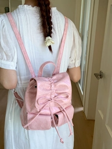 Pink faux leather backpack with bow detail worn by a model in a soft indoor setting