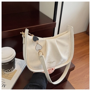 Détail du sac bandoulière plissé crème avec chaîne cœur et texture cuir sur bureau en bois