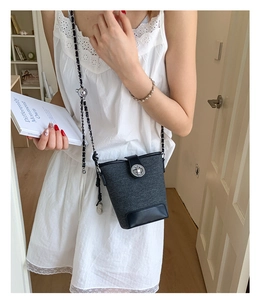 Detail of a mini bucket bag featuring textured grey fabric and black leather trim