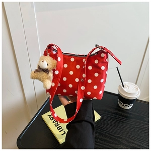 Detail einer roten gepunkteten Stoffhandtasche mit süßem Teddybär-Anhänger auf Tisch