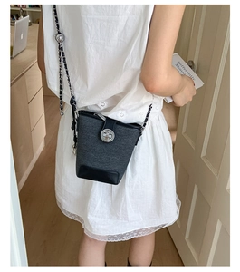 Detail view of a black bucket bag with a metal twist lock and chain strap on a model