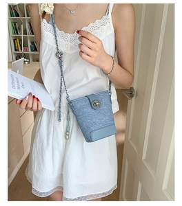 Detail of light blue denim bucket bag featuring silver twist lock and braided chain strap