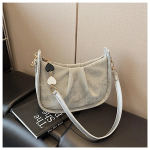 Détail du sac plissé gris avec breloques cœur posé sur une surface en cuir noir