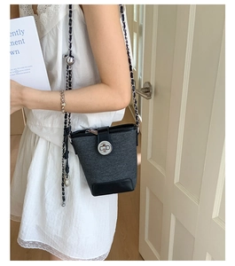 Detail of tweed bucket bag with black leather base and silver chain strap on model