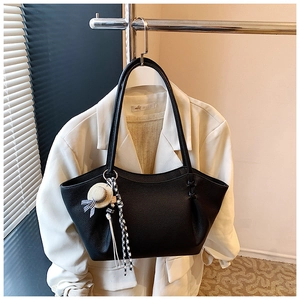 Detail of black pebbled leather tote bag featuring a decorative straw hat pendant and bow