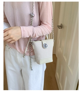 Detail of a creamy canvas bucket bag with metal chain strap and adjustable golden ball
