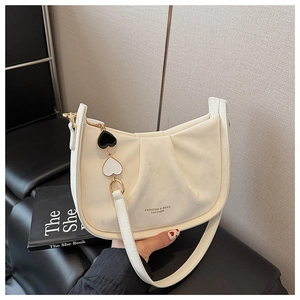 Détail du sac hobo plissé blanc cassé avec logo et charms en forme de cœur, tenu à la main