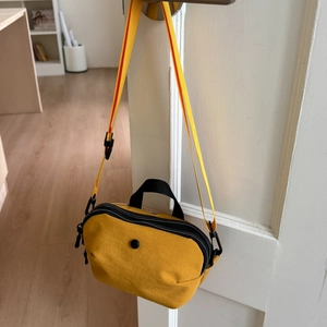 Detail view of yellow nylon crossbody bag with black zippers and woven shoulder strap
