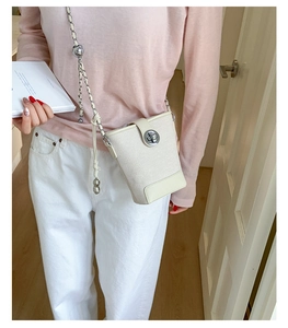 Detail of off-white bucket bag featuring metal chain strap and twist lock on model