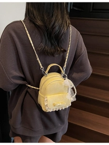 Mini sac à dos jaune avec dentelle blanche, nœud et chaîne sur un escalier en bois