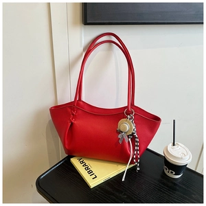 Detail of red litchi grain leather tote bag with mini straw hat and ribbon charm accessory