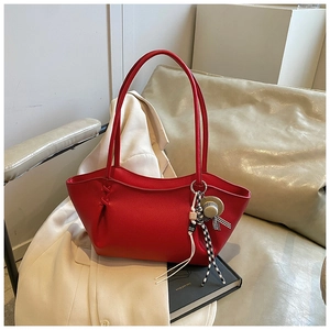 Detail of red lychee leather tote bag with elegant charm and decorative side pleats